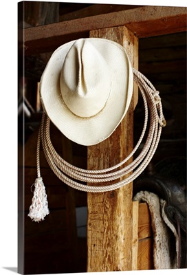 Cowboy hat hanging in barn with rope.