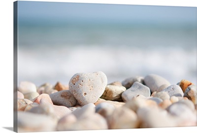 Directed focus on a heart shaped stone on a pebble beach in the foreground.