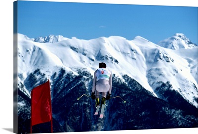Downhill skier in mid-air jump, mountains in background, rear view