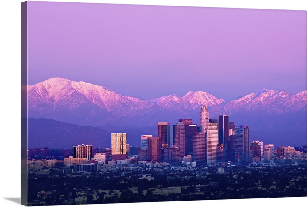 Downtown Los Angeles and sunset. Buildings are lit from setting sun and mountains are capped with snow in distance. Tones ...