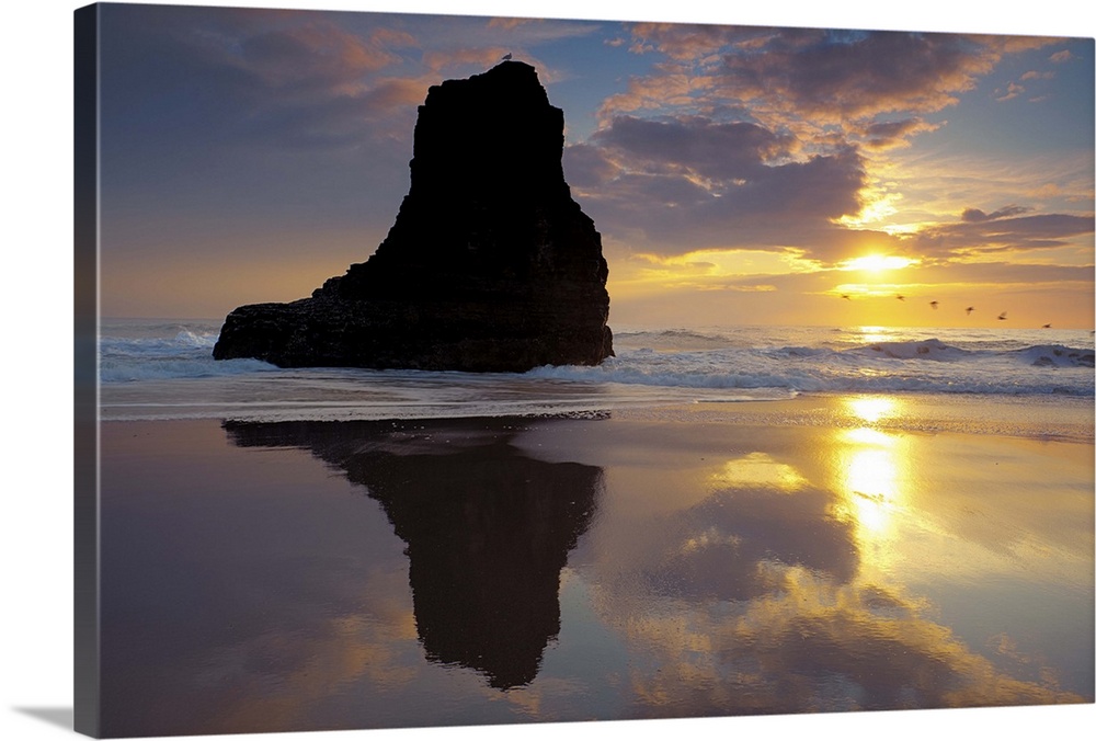 Sunset and seastack reflecting off wet sands at San Vicente Beach in Davenport, CA.