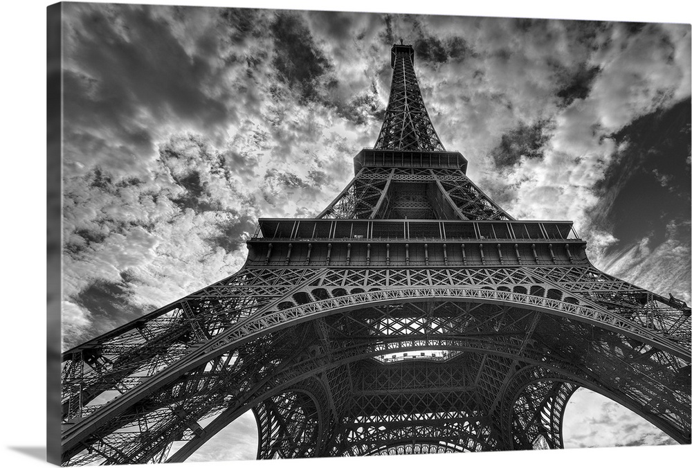 Landscape, low angle photograph looking up one side of the Eiffel Tower, the background is a sky full of small, fluffy clo...