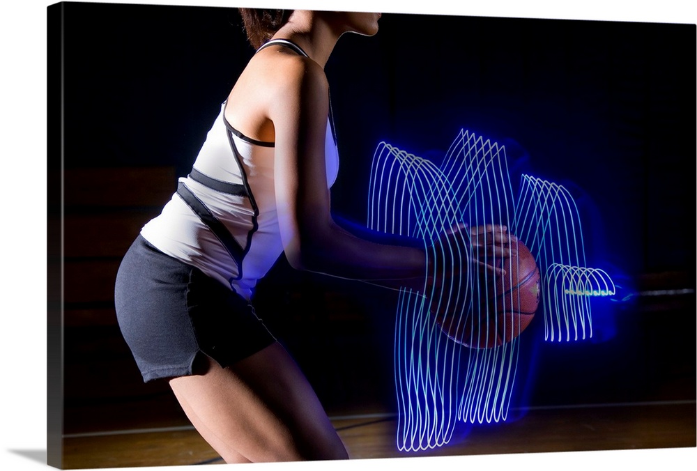 Female basketball player holding ball with surrounding light trail, side view, mid section, digital composite