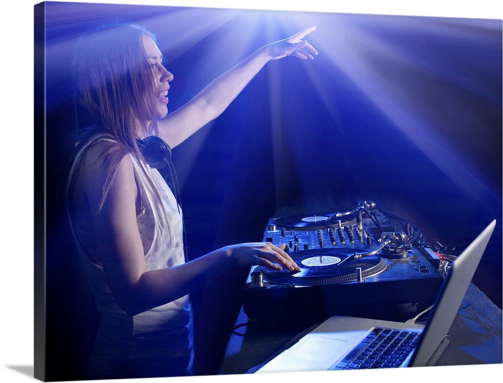 Female DJ using decks and laptop, reaching out to audience, surrounded by bright lights