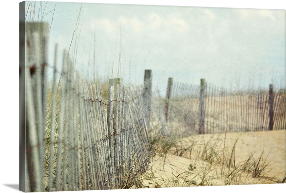 Photograph of wooden fence and tall grass on hills of sand at the coast under cloudy skies.