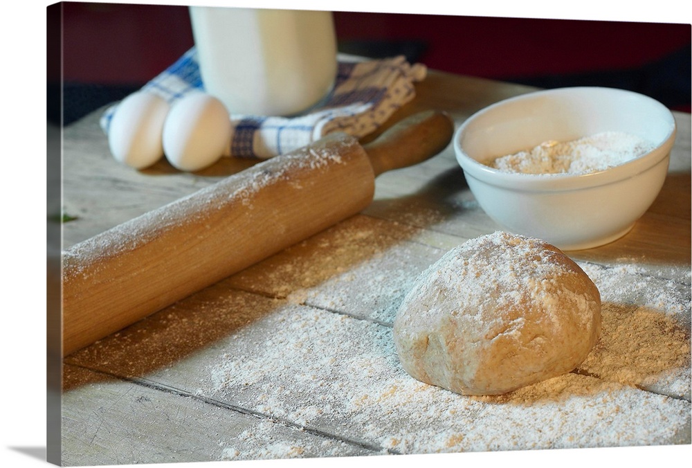 Large horizontal photograph of bread dough in ball on a wooden table, sprinkled with flour.  Objects also sitting on the t...