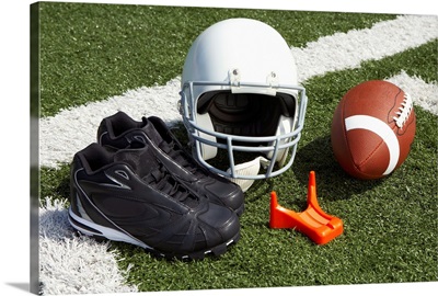 Football, football helmet, tee and shoes on football field