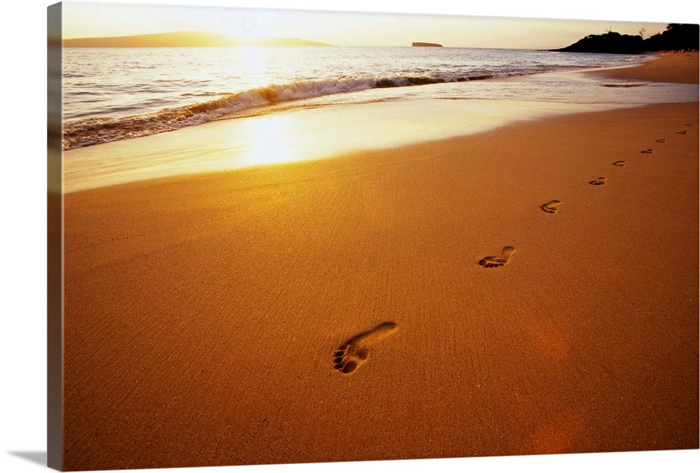 Footprints along Makena Beach on Maui. The setting sun reflects off the sand and surf.