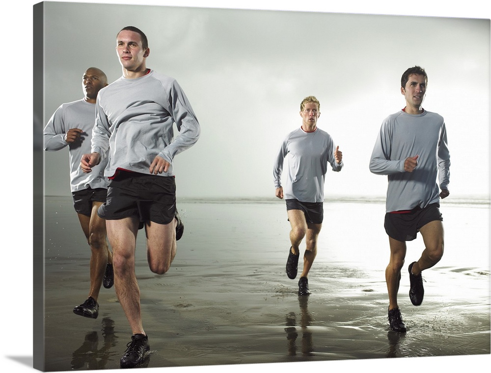 Four men running on beach by ocean