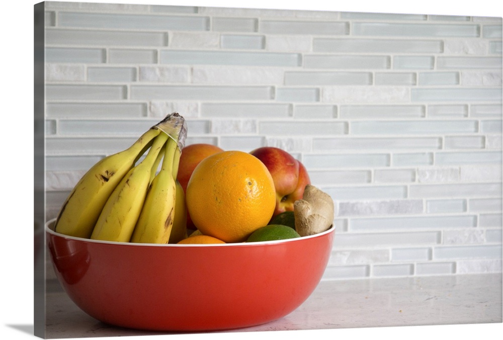 Red bowl with fresh fruit on grey granite kitchen counter with glass tile backsplash.