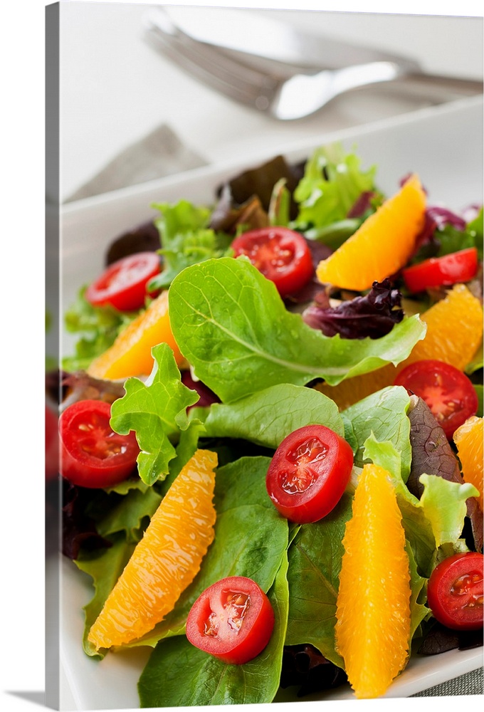 Leafy greens topped with tomatoes and oranges is elegantly photographed.