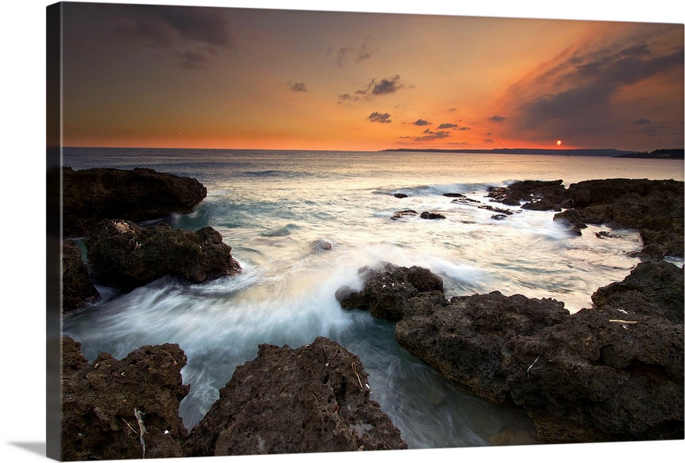 Frog Rock, kenting at dusk with foaming waves rushing in and crashing on dark coral reefs while sky is painted red by sett...