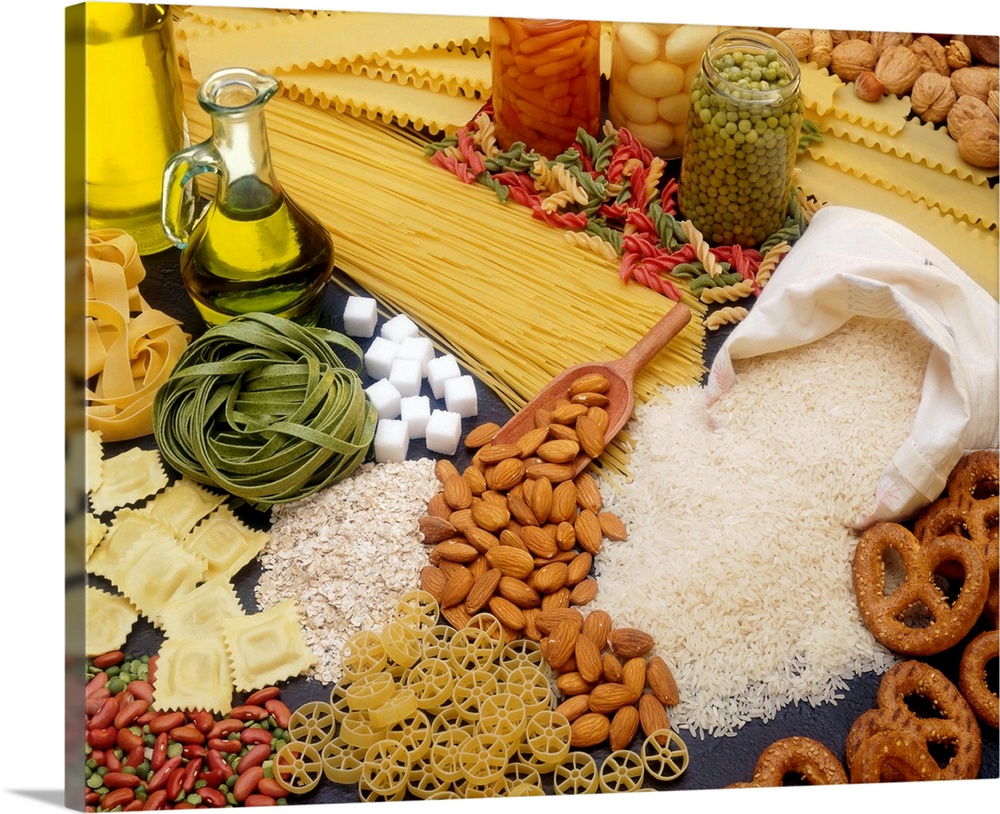 All different types of pasta, nuts and beans are scattered about on a flat surface.