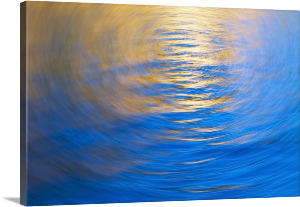 Gently rippled water reflecting gold and blue colours, vortex.