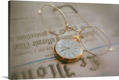 Glasses and clock on newspaper, high angle view, close up, soft focus