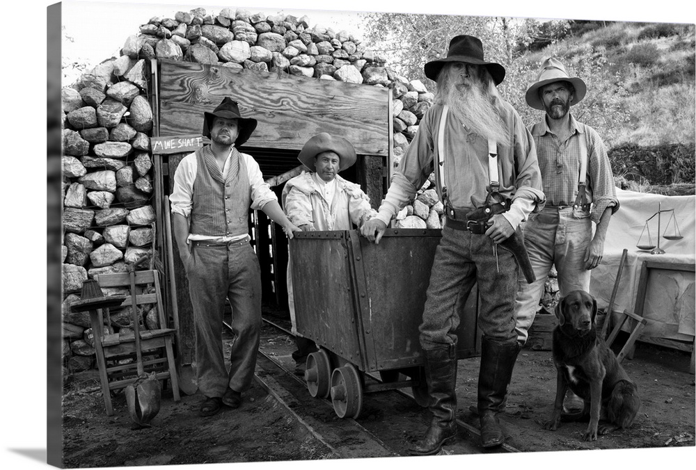 Four men, gold miners and cowboys in front of a mine shaft with a dog