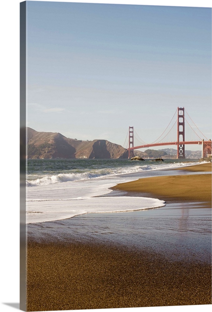 Vertical photograph taken from a distance of the Golden Gate Bridge which a strip of beach and the ocean pictured in the f...