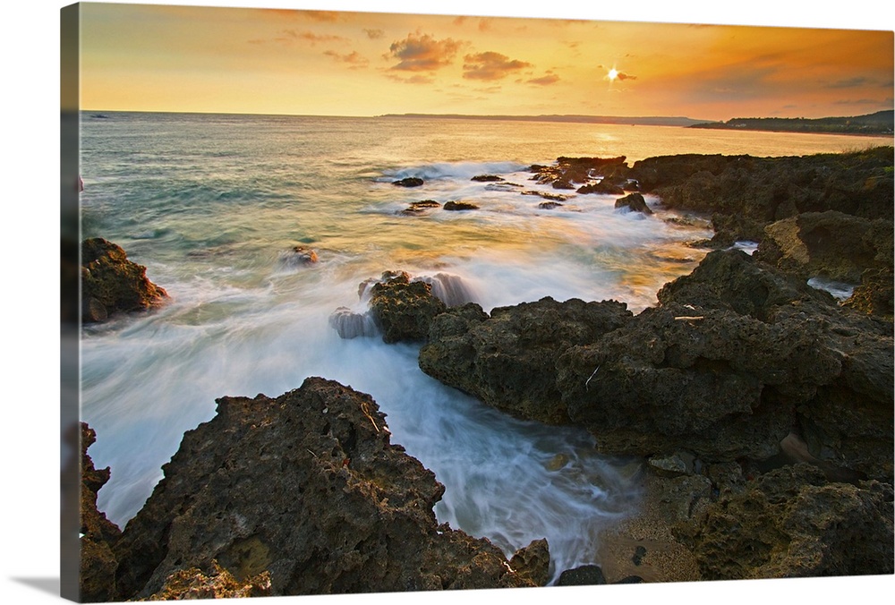 Frog rock in Kenting at golden dusk with foaming waves rushing in and crashing on dark coral reefs while setting sun paint...