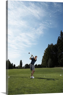 Golfer swinging club on golf green, side view