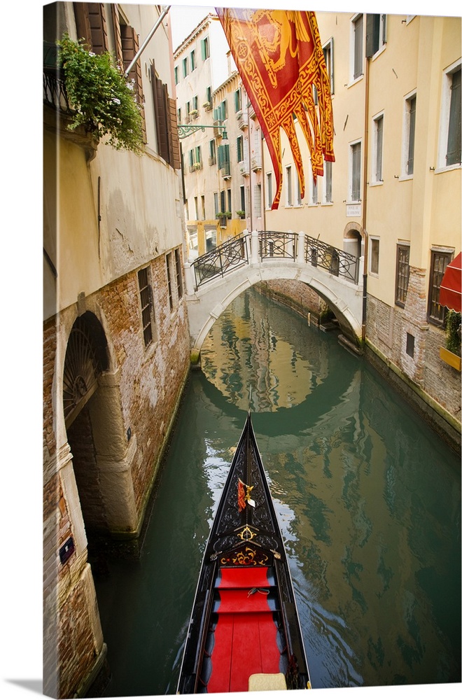 Solitary gondola in narrow canal about to pass under a pedestrian bridge