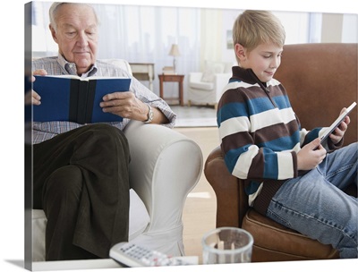 Grandfather reading book, grandson  reading e-book in living room