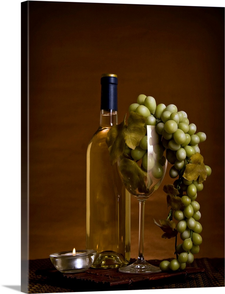 Wine bottles with grapes in wine glass and small candle.