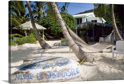 Hammock between palms, upturned boat and houses on beach