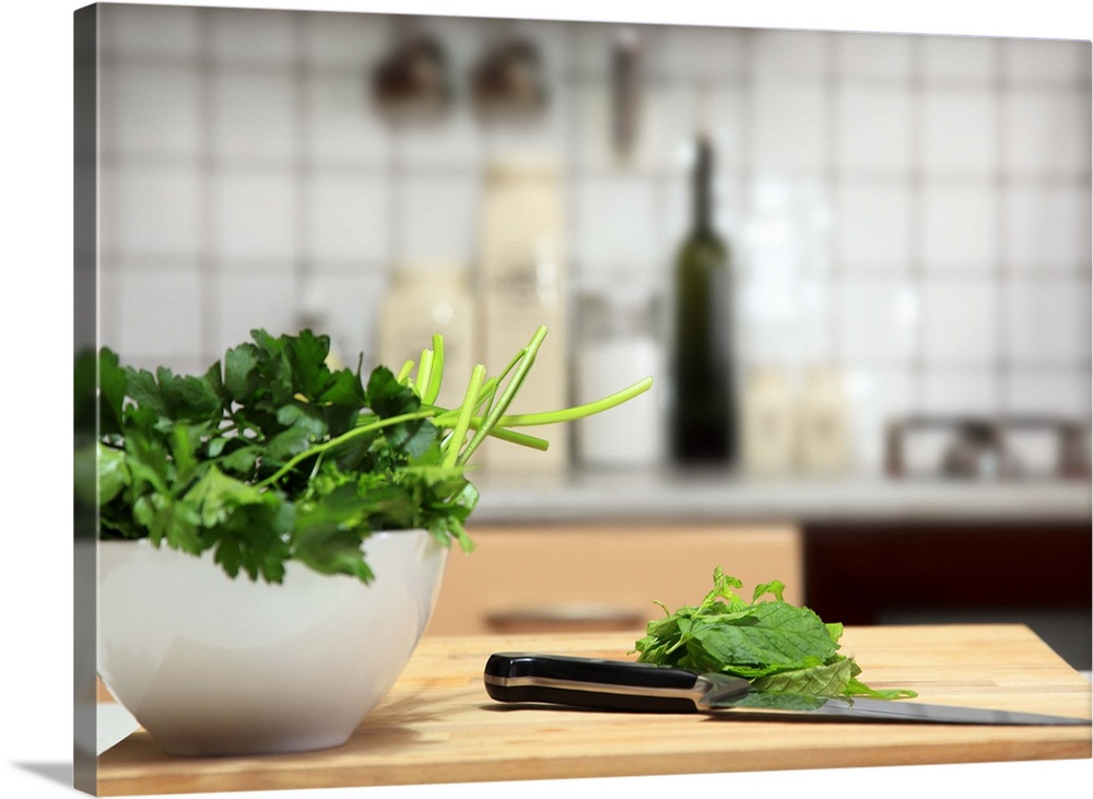 Basil and parsley on a white bowl. There are also some herbs on a wooden surface, ready to be cut. There is also a chef kn...