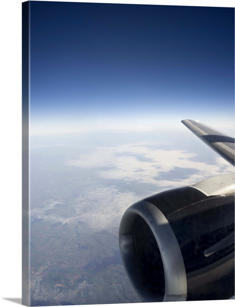 High altitude view of a jet engine set against a gentle cloudscape with the outline of land and coastline visible beneath ...