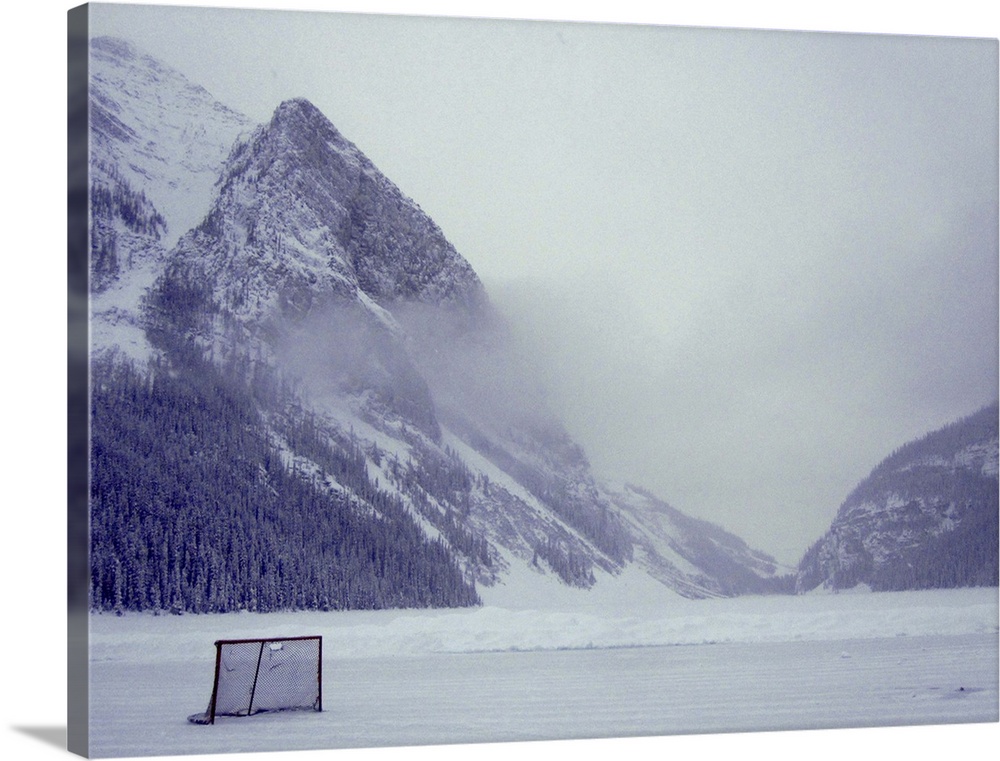 A lone hockey net stands on Lake Louise in the early morning mist. The famous glacier lurks behind the clouds.