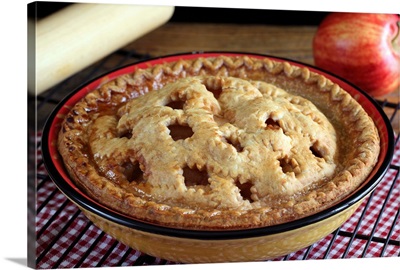 Home baked apple pie on cooling rack with apple and rolling pin