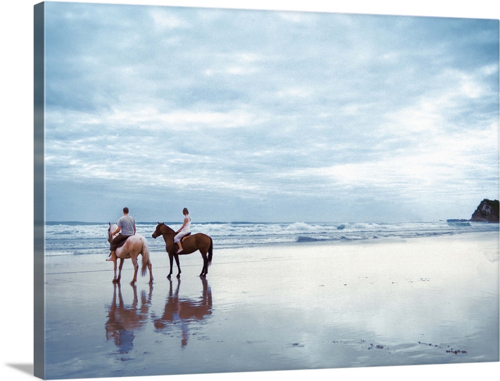 A couple riding horses on Parkiri beach in New Zealand.