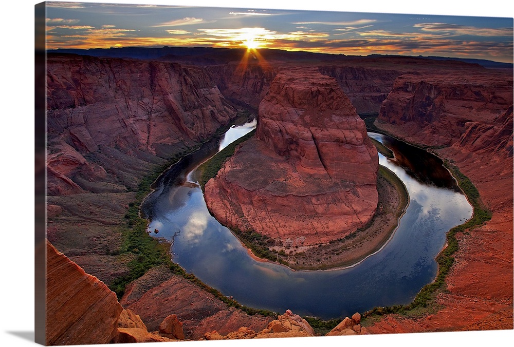 Photograph of river circling huge rock formation at sunset under a cloudy sky.