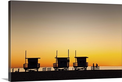 Huts and people silhouetted at sunset on Venice Beach