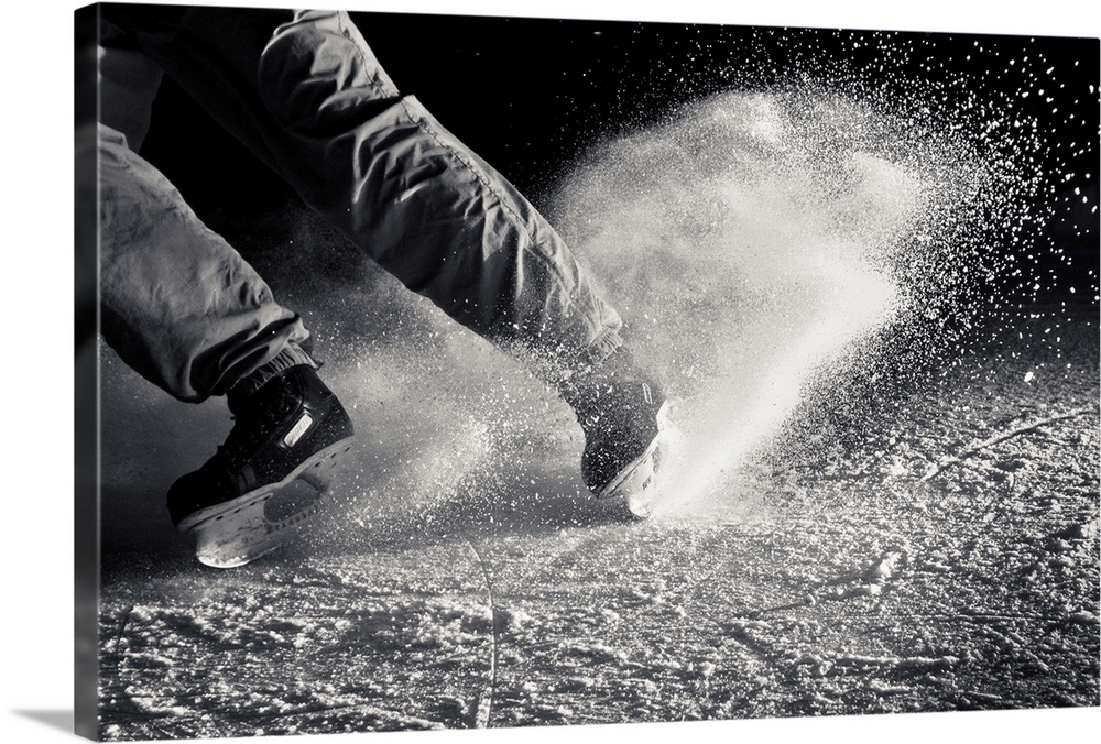 Black and white view of human legs doing ice skating with ice particles.