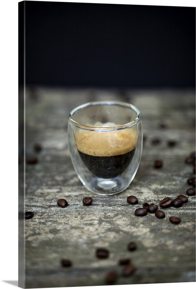 Close-up of typical espresso coffee in glass cup amongst raw coffee beans on wooden table and black background