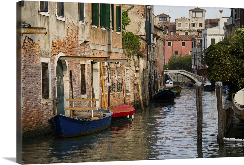A picture of a canal is taken with boats docked on the left side where buildings line the water.