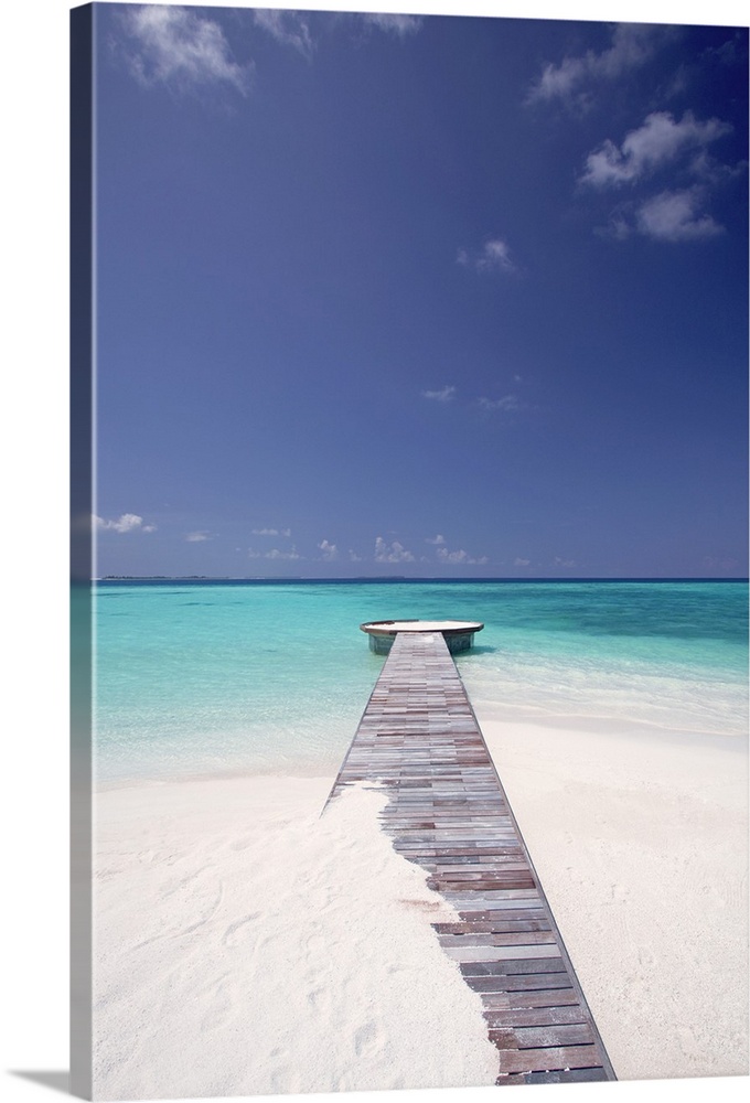 Vertical photo of a wooden walkway stretching out into the tropical sea, partly covered in sand.