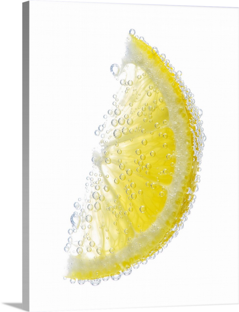 A juicy ripe organic lemon wedge fruit submerged in clean clear refreshing water and covered in bubbles on a white backgro...