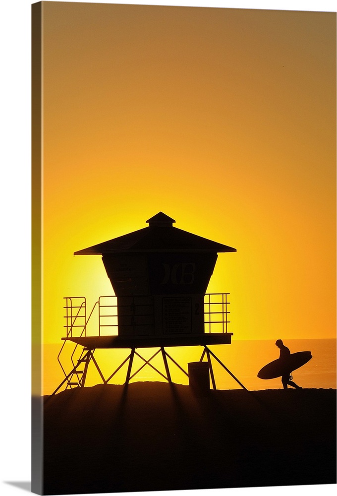 Surfer and Lifeguard tower silhouetted against setting sun.