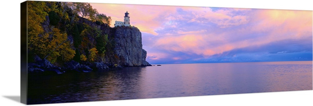 Panoramic photo print of a lighthouse on top of a cliff overlooking the water at sunset.