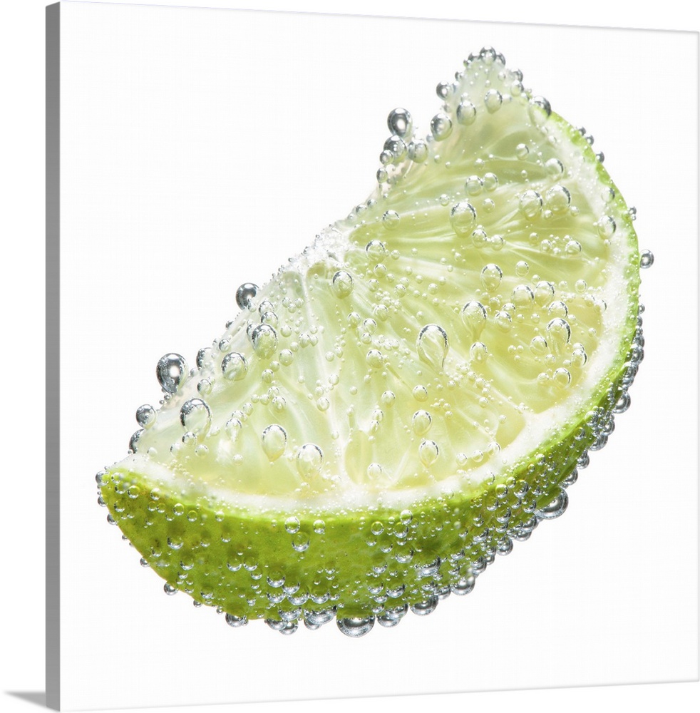 A juicy ripe organic lime wedge fruit submerged in clean clear refreshing water and covered in bubbles on a white backgrou...