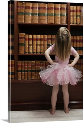 Little girl in tutu reading book covers in library