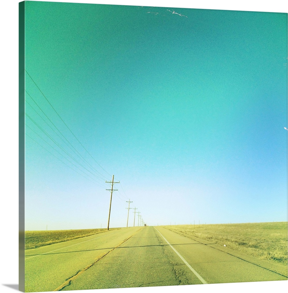 Lone car on simple country road with clear blue sky and telephone lines.