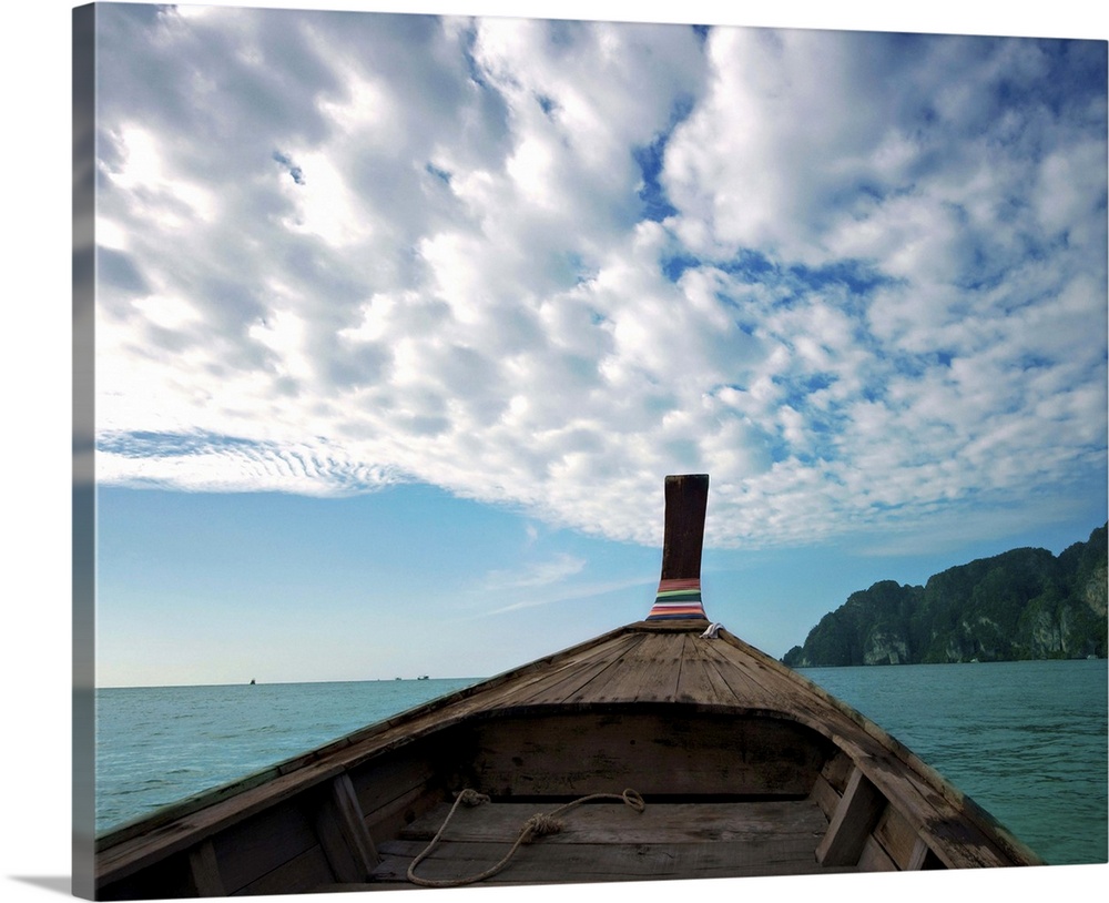 Long boat in sea with cloudy sky and mountain in background.
