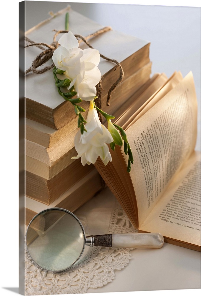 Magnifying glass beside stack of books with flowers