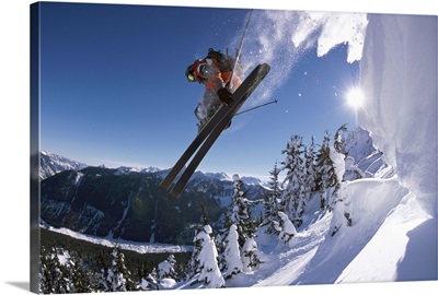Male skier jumping off snow cornice, holding skis, low angle view