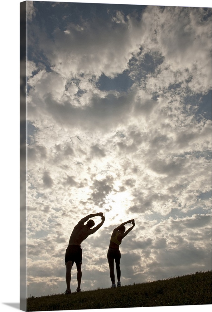 Oversized, portrait photograph of a man and woman standing next to each other, stretching their arms and backs, silhouette...