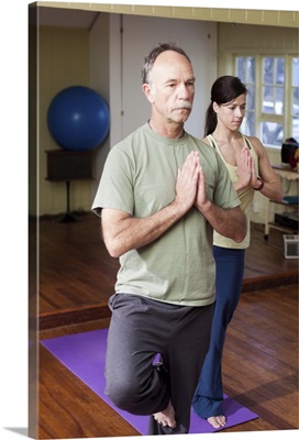 Man in front of a younger woman practices a yoga position in a small studio