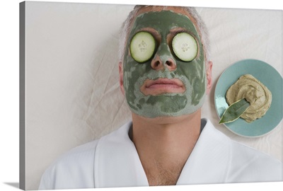 Man lying down with a face pack and cucumber slices on his eyes